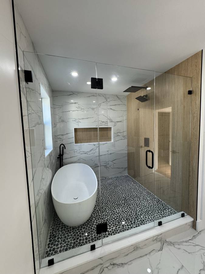 Glass-enclosed wet room with freestanding tub, pebble floor and wood accent wall — Nexus Pro Construction