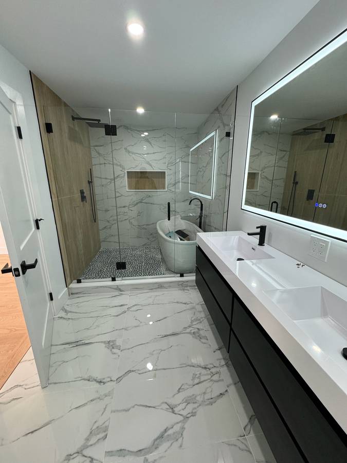 Bathroom with marble-look floor, black double vanity, lit mirror and soaking tub — Nexus Pro Construction