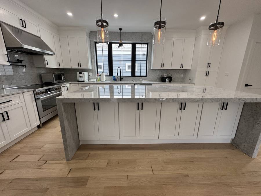 White shaker kitchen with waterfall marble island and wide-plank oak floor — Nexus Pro Construction